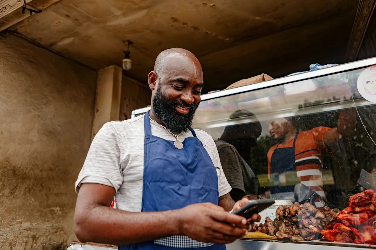 A Zimbabwean street-food vendor smiling as he checks a payment on his phone